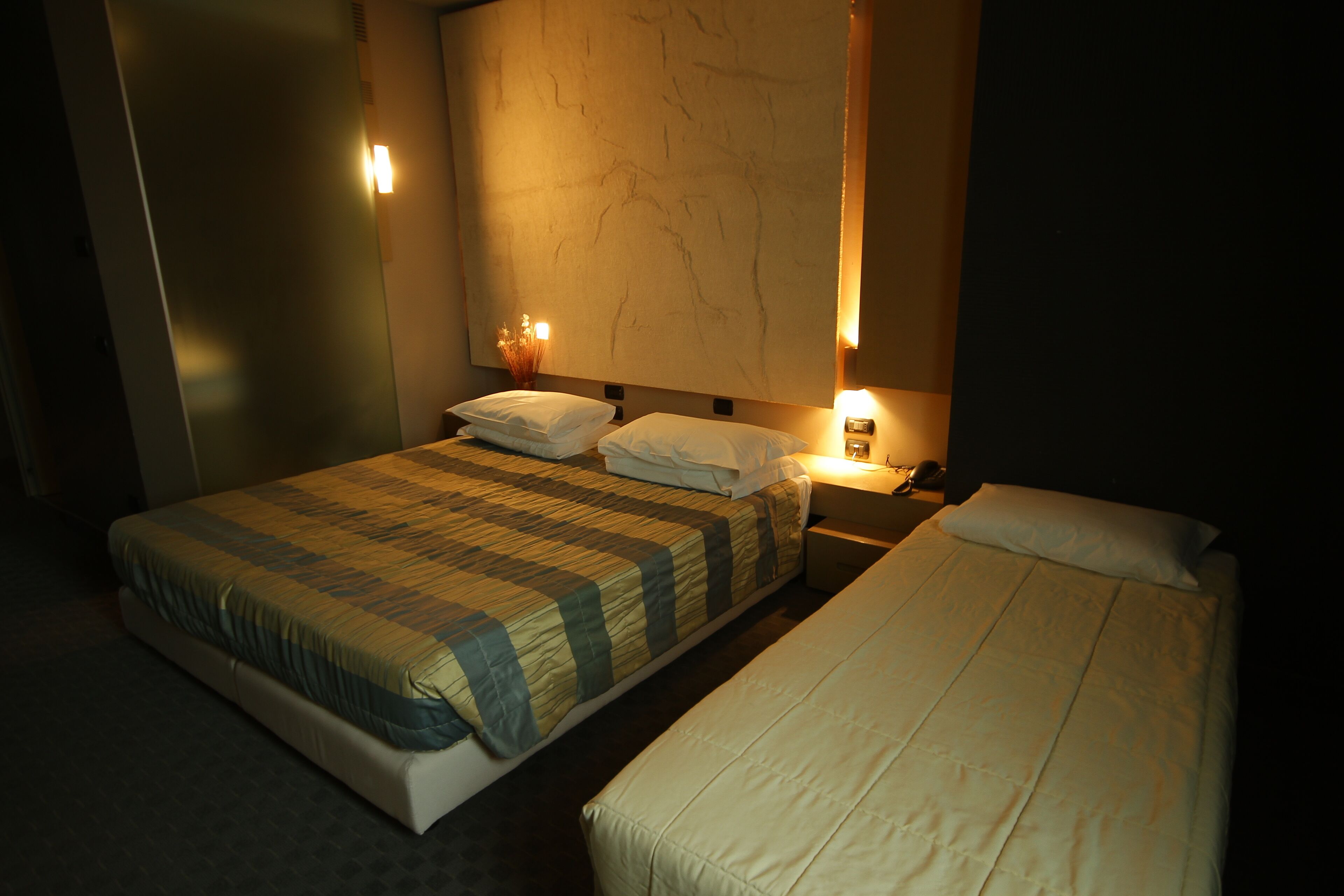 Ein Hotelzimmer mit einem großen Bett, einem kleineren Bett und einem Nachttisch mit einer Lampe.