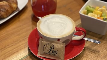 Une table avec une tasse de café, un verre d’une boisson rouge, une pâtisserie et un bol de fruits.