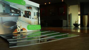 Een hotel receptie met een modern design, inclusief een receptiebalie en een grote poster die BES HOTEL in Cosenzo en Cremona promoot.