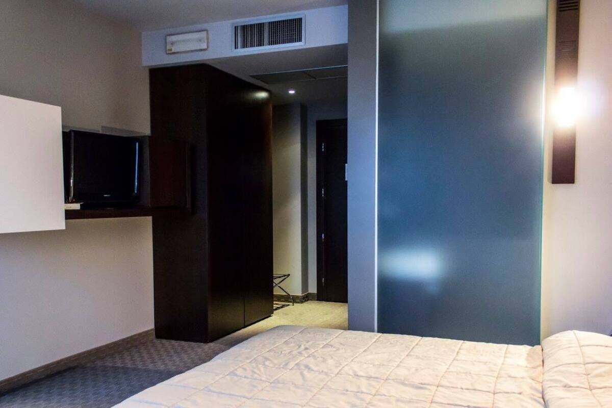 Habitació d'hotel amb llit, televisió penjada a la paret i armari.