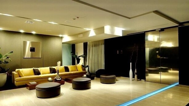 Una sala moderna con un sofá amarillo, otomanos redondos y un suelo iluminado en azul.