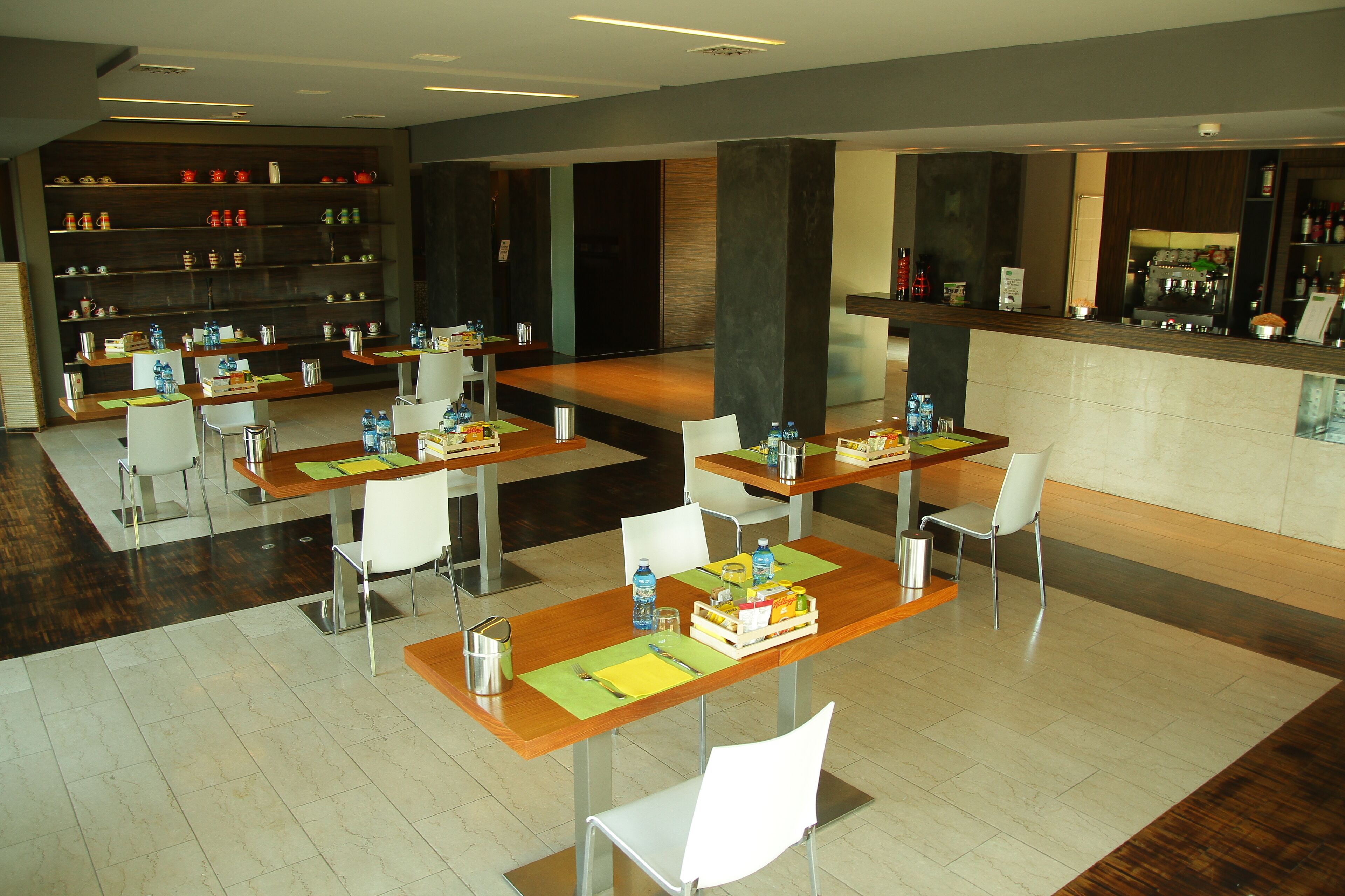 Un restaurante moderno con varias mesas y sillas, una zona de bar y estanterías con diversos artículos.