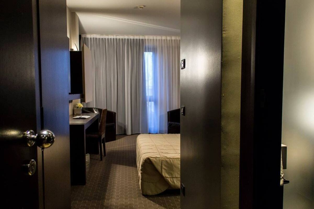 Una habitació d'hotel amb llit, escriptori, cadira i finestra amb cortines.