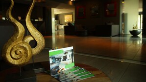 Un área de recepción de diseño moderno, con mostrador de recepción, una gran escultura decorativa y un atril para folletos.