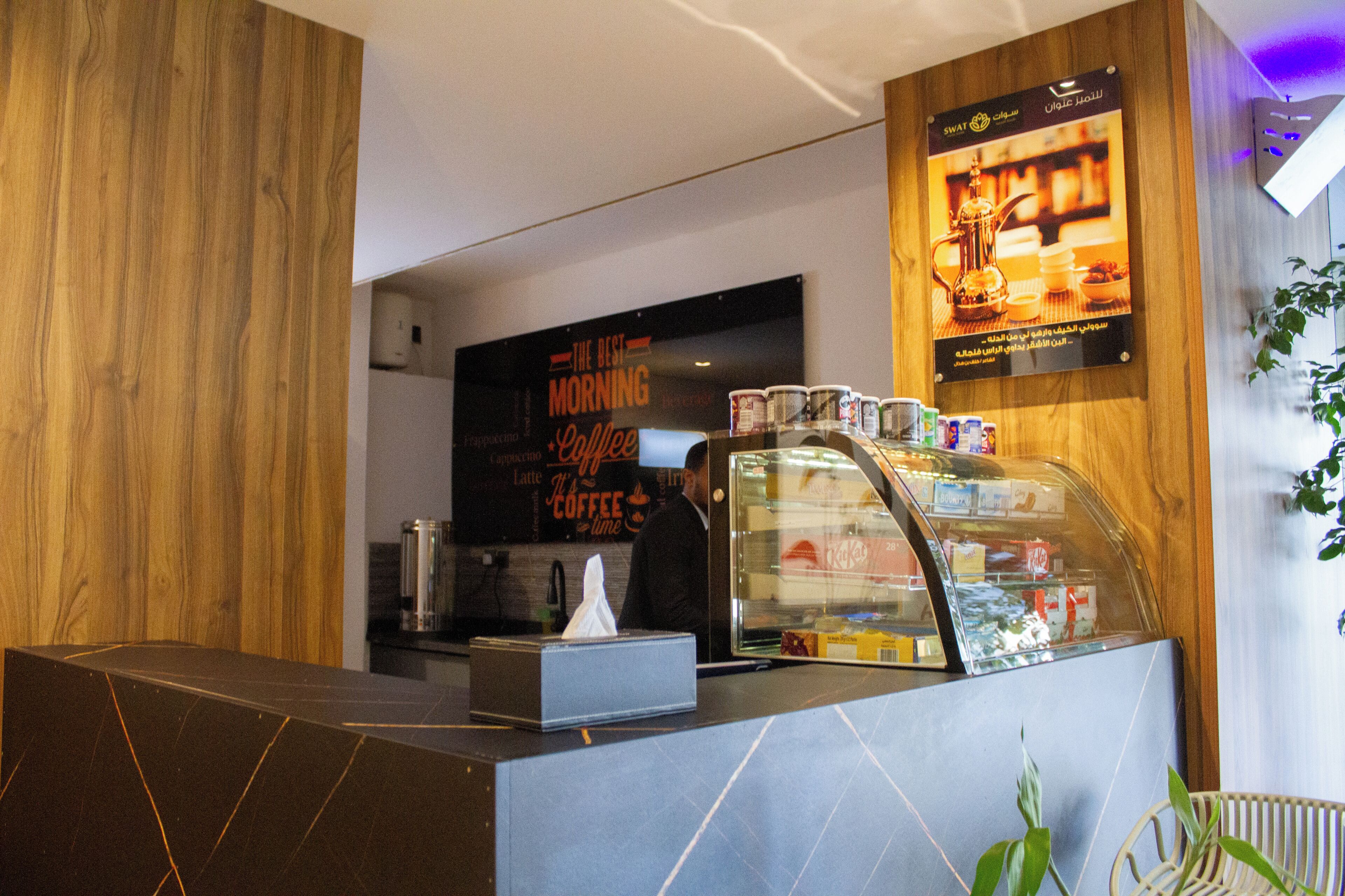 A coffee shop interior with a counter, a display case with coffee products, and a wall with a coffee-themed sign.