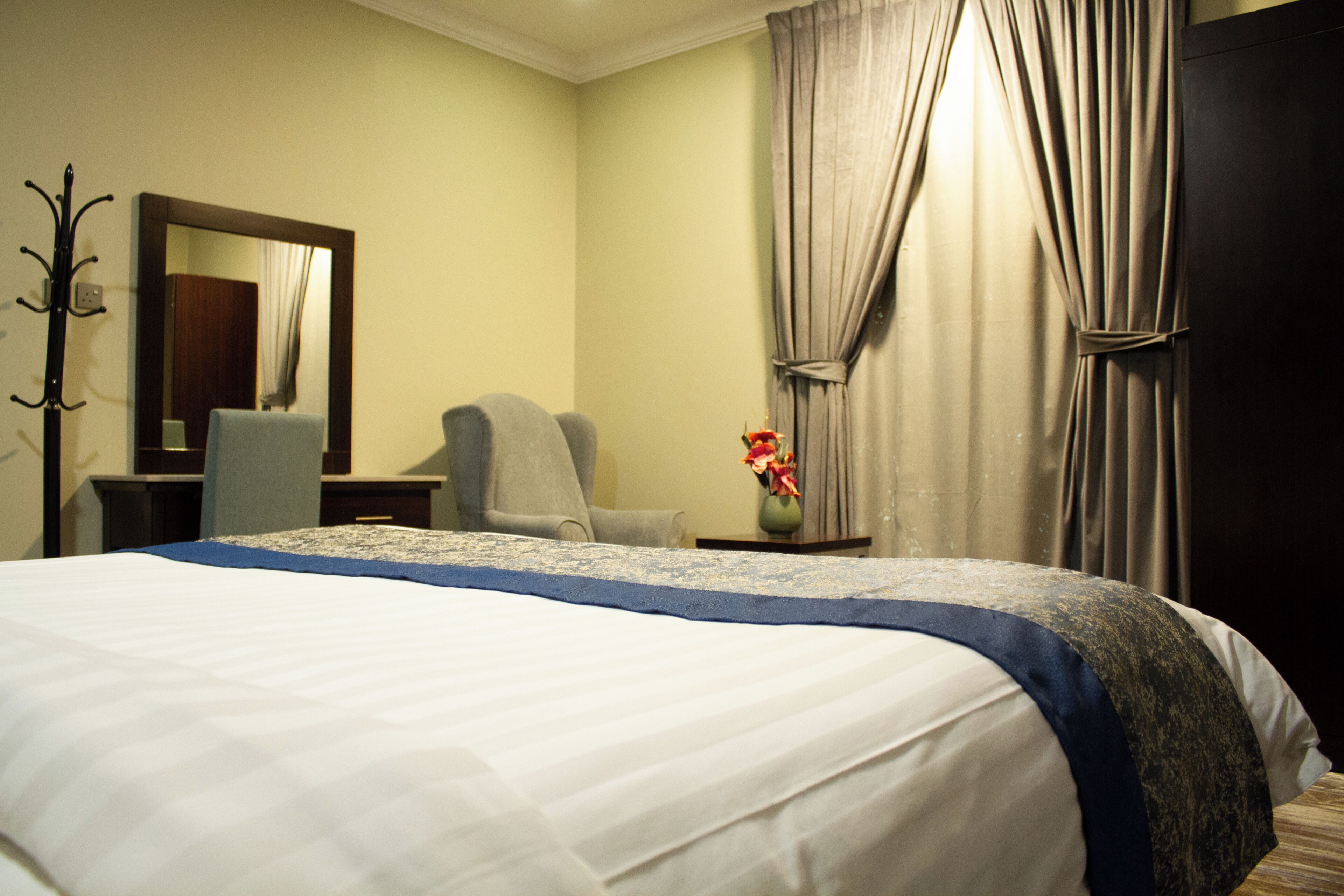 Una habitación de hotel con una cama, una silla, un escritorio, un espejo y un florero con flores.