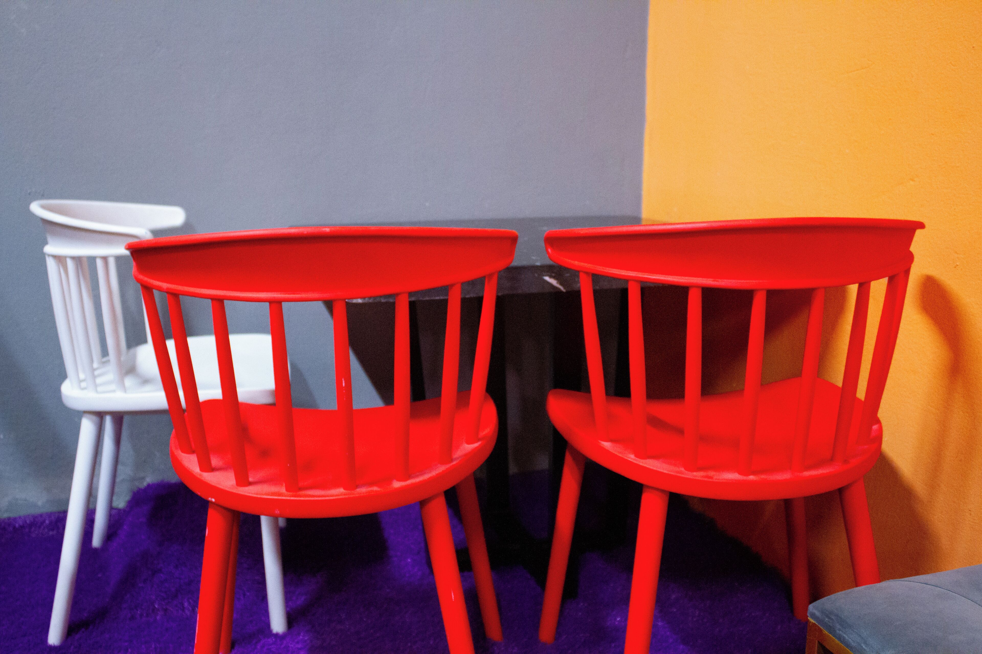 Two red chairs with a white chair and a black table in a room with purple carpet and a grey and yellow wall.