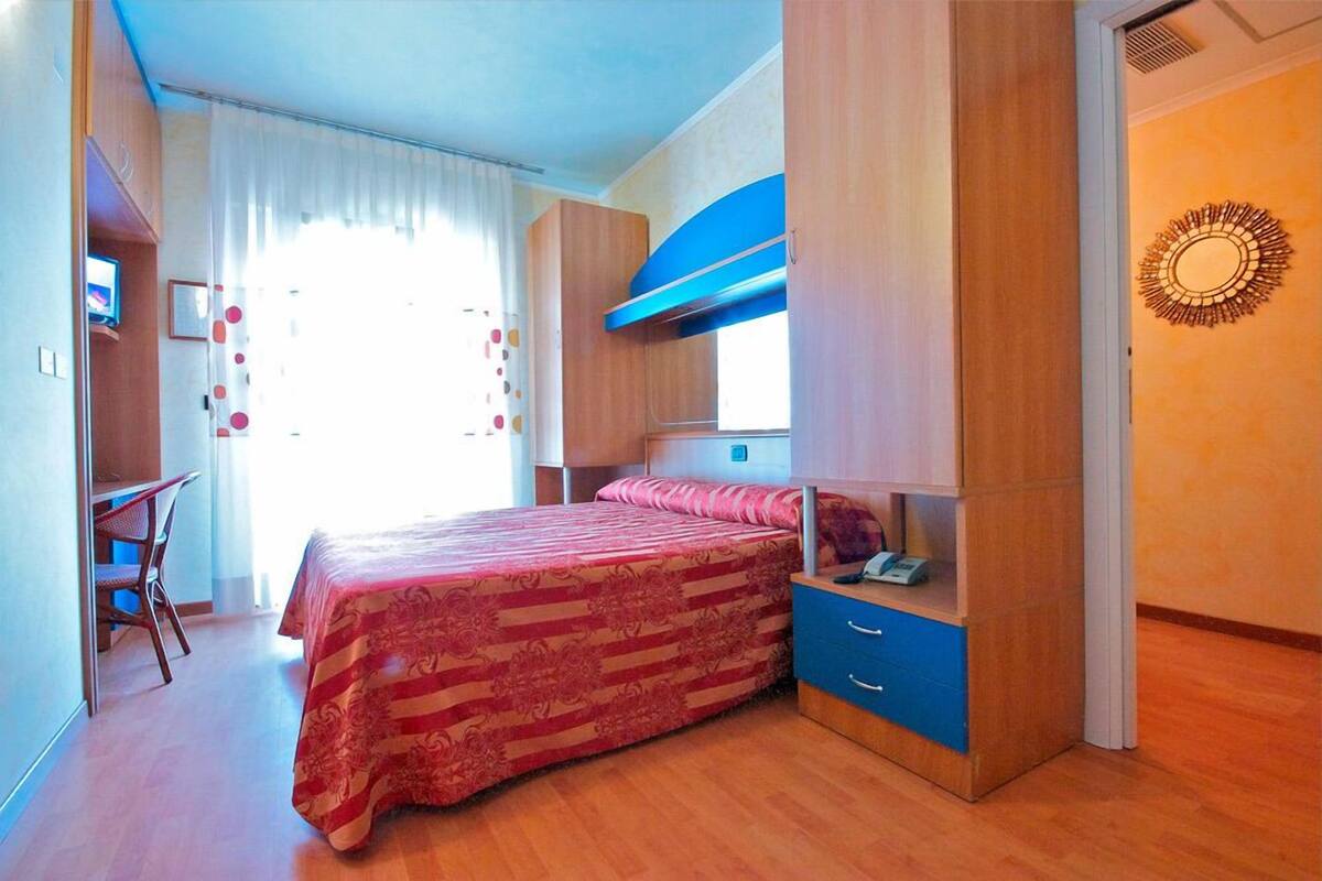 A bedroom with a bed, a desk, and a wardrobe.