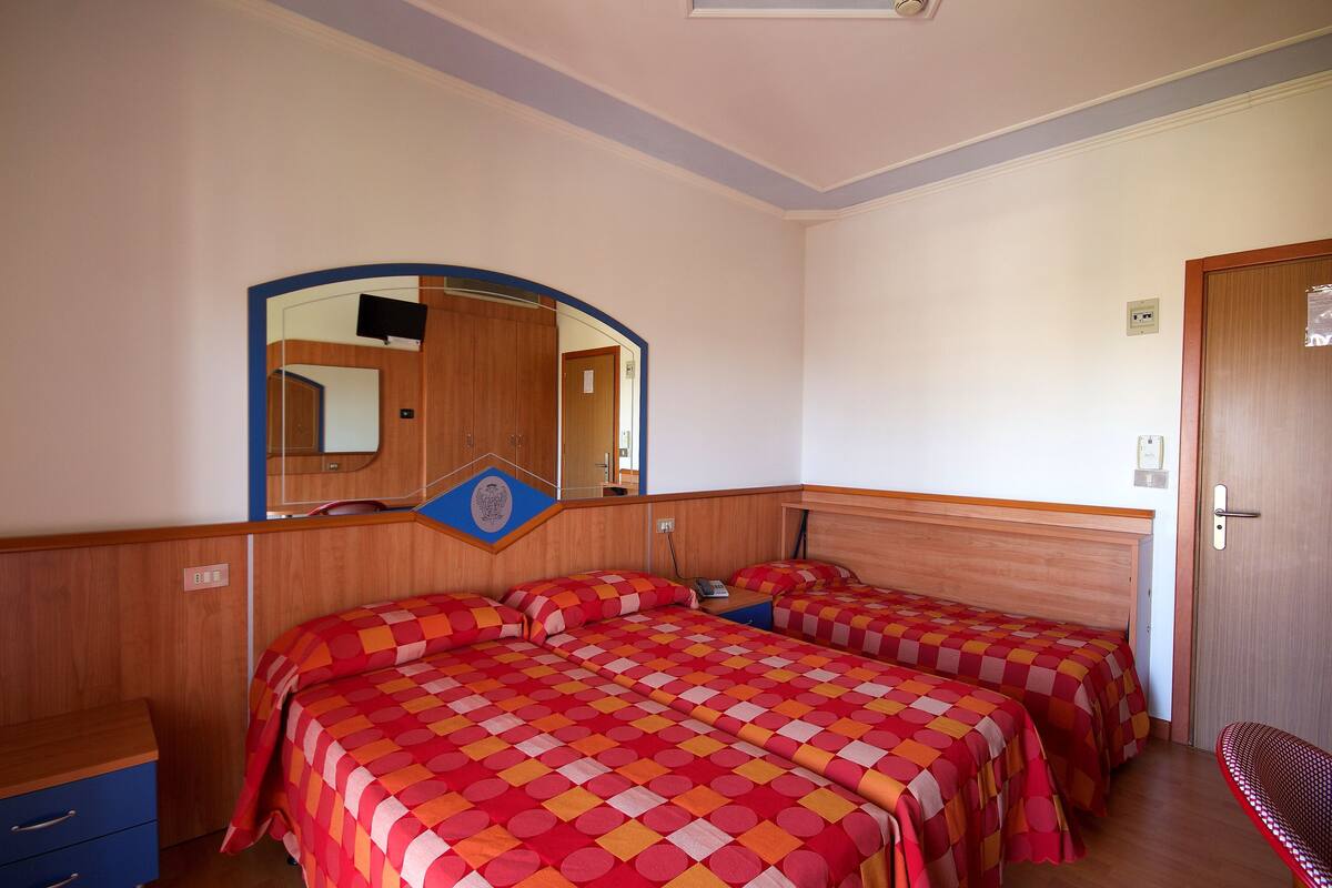 Una habitación de hotel con dos camas, un armario de madera, un espejo y una puerta.