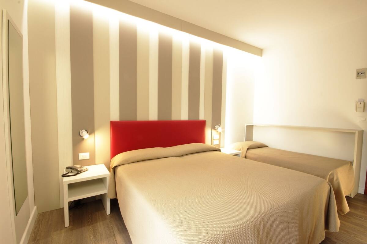 A hotel room with two beds, a striped wall, and bedside lamps.