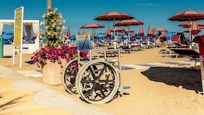 A beach with wheelchairs, umbrellas, and a flower bed. - Hotel Toledo (Jesolo)