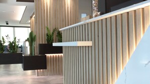 A reception area with a modern design, featuring a reception desk, vertical wooden slats, and potted plants. - Hotel Toledo (Jesolo)