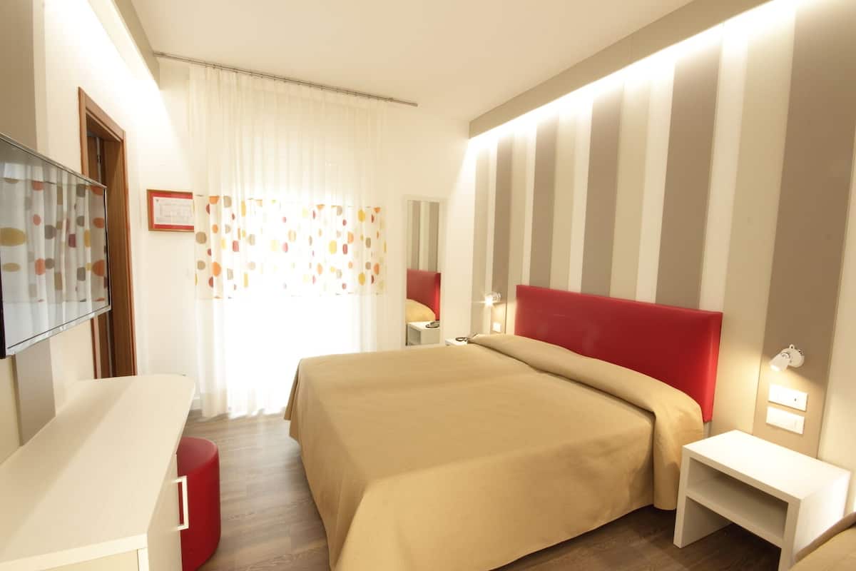 A hotel room with a bed, a desk, a chair, a nightstand, and a mirror.