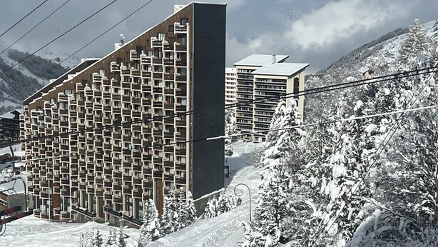 Ein modernes Hotel mit einer rasterförmigen Fassade, umgeben von schneebedeckten Bäumen und Bergen.