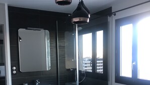 Ein modernes Badezimmer mit einem weißen Waschtisch, einer Duschkabine aus Glas und einem großen Spiegel.