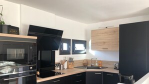 Eine kleine Küche mit schwarzen Schränken, einer Mikrowelle, einem Backofen, einem Spülbecken und einem Fenster.
