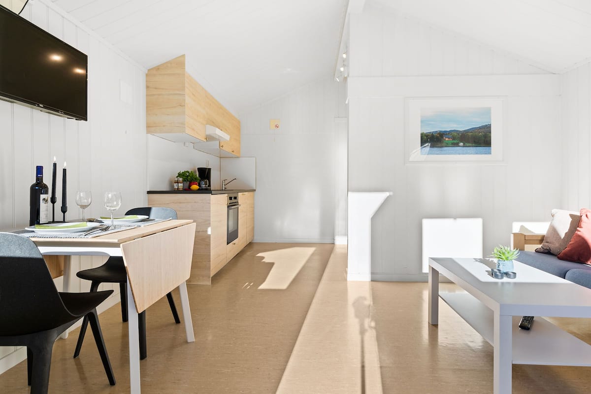 A modern kitchen with a dining area, a sofa, and a view of a landscape through a window.