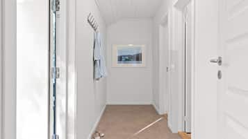 A narrow hallway with white walls, a small window with a view, and a door on the right.