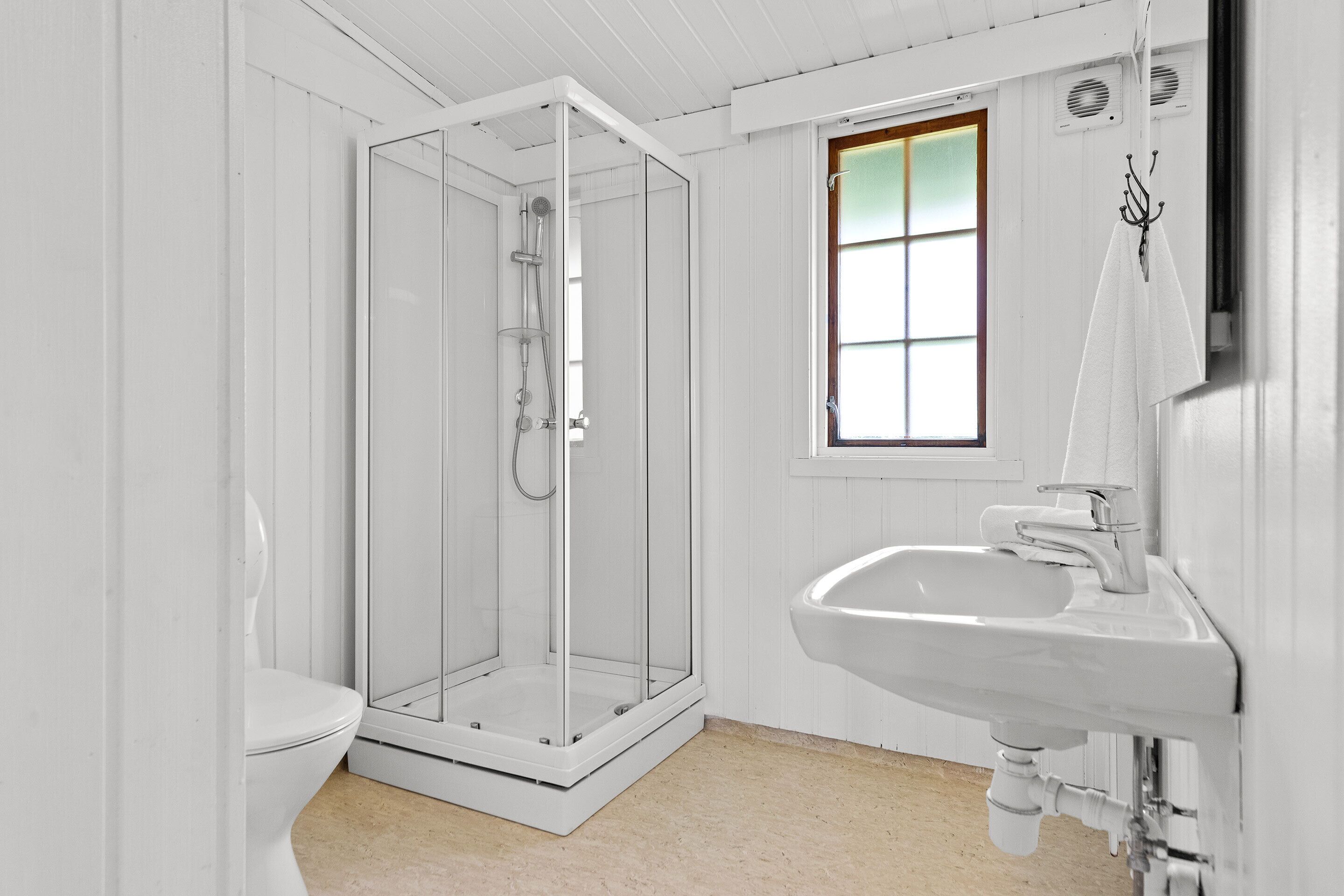 A bathroom with a glass-enclosed shower, a white sink, and a window with a view.