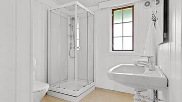 A bathroom with a glass-enclosed shower, a white sink, and a window with a view.