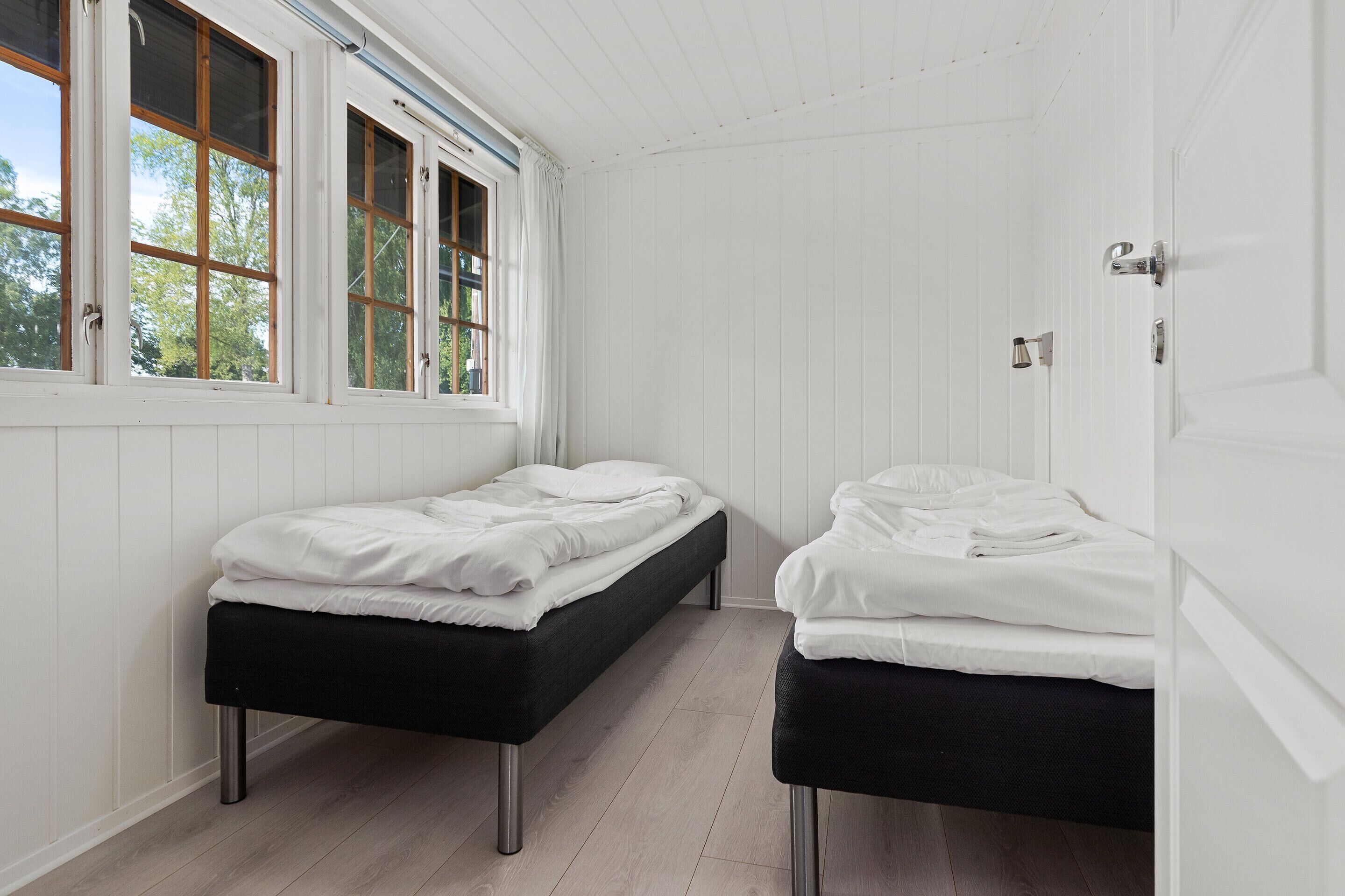 Una habitación con dos camas, paredes blancas y suelo de madera.