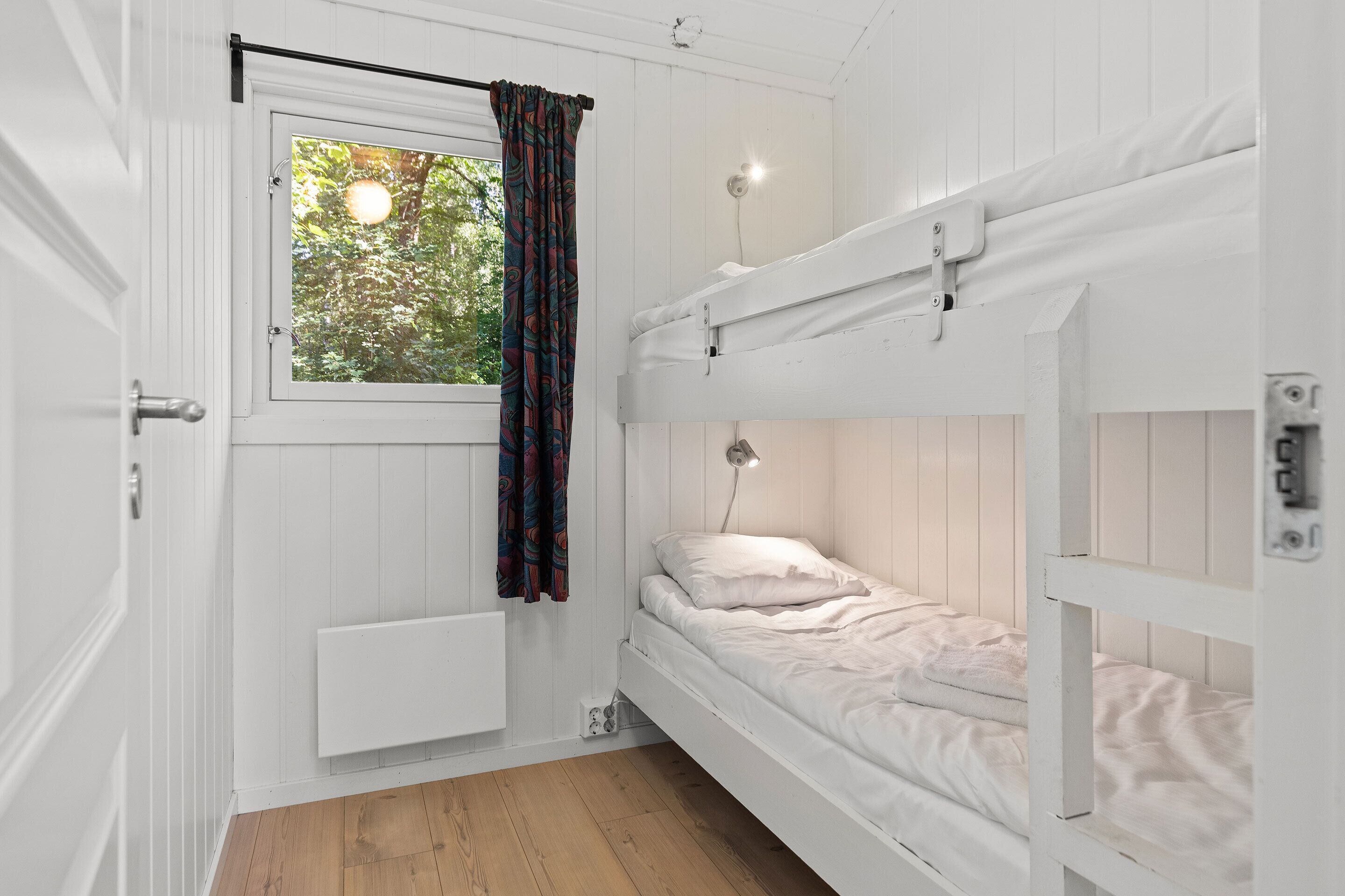 A room with a bunk bed, a window with a curtain, a radiator, and a light fixture.