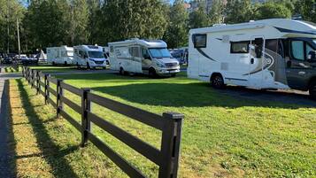 A row of RVs parked on a grassy field with a wooden fence in the foreground.