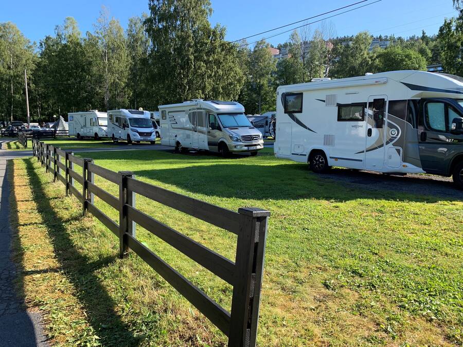 A row of RVs parked on a grassy field with a wooden fence in the foreground.