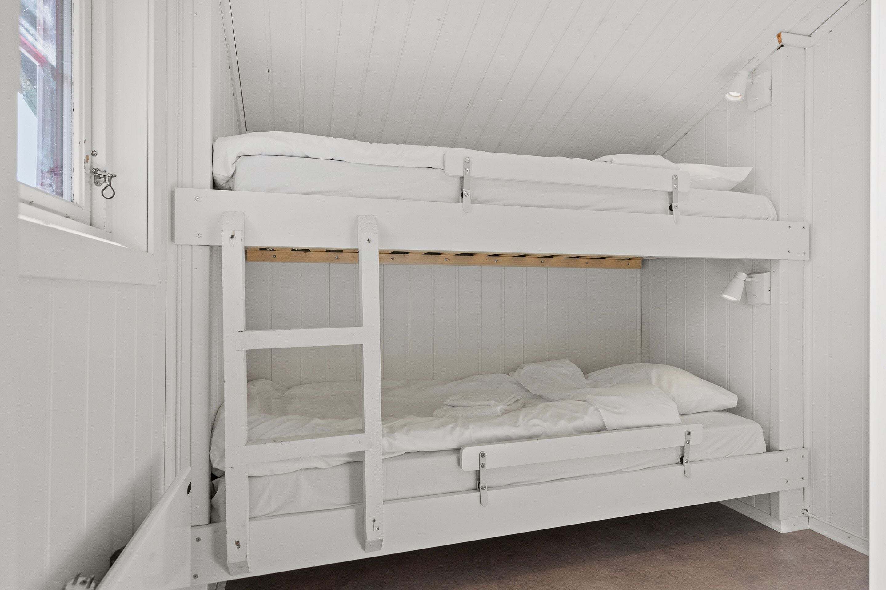 A bunk bed with white bedding and a wooden ladder.