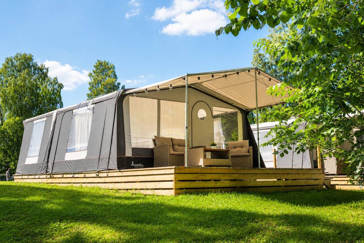 A mobile home with a covered porch, outdoor seating, and a view of the surrounding greenery.