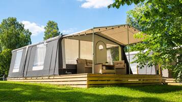 A mobile home with a covered porch, outdoor seating, and a view of the surrounding greenery.