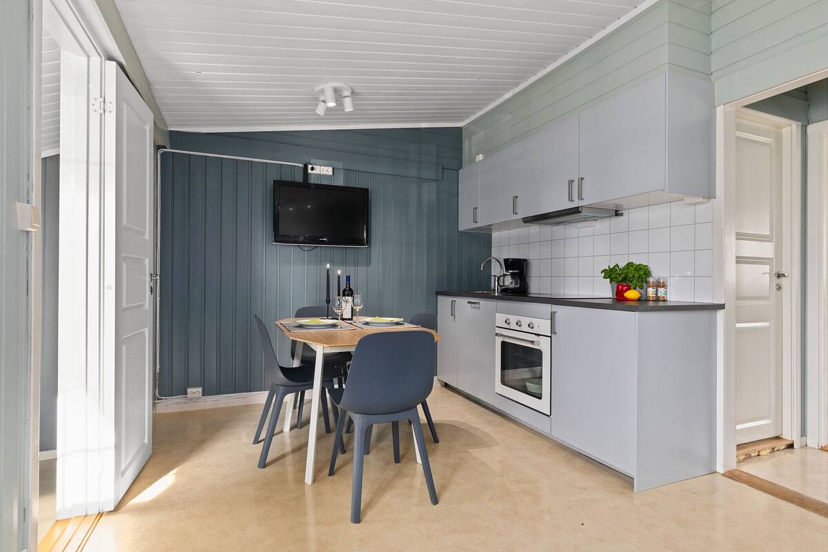 A compact kitchen with a dining area, a TV mounted above the table, and a small island with a coffee maker.