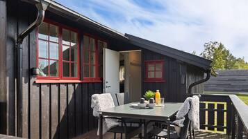 A wooden deck with a table and chairs, a red-framed window, and a door leading to an interior space.