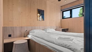 A modern bedroom with a wooden wall panel, a bed with white linens, a bedside table, and a small stool.