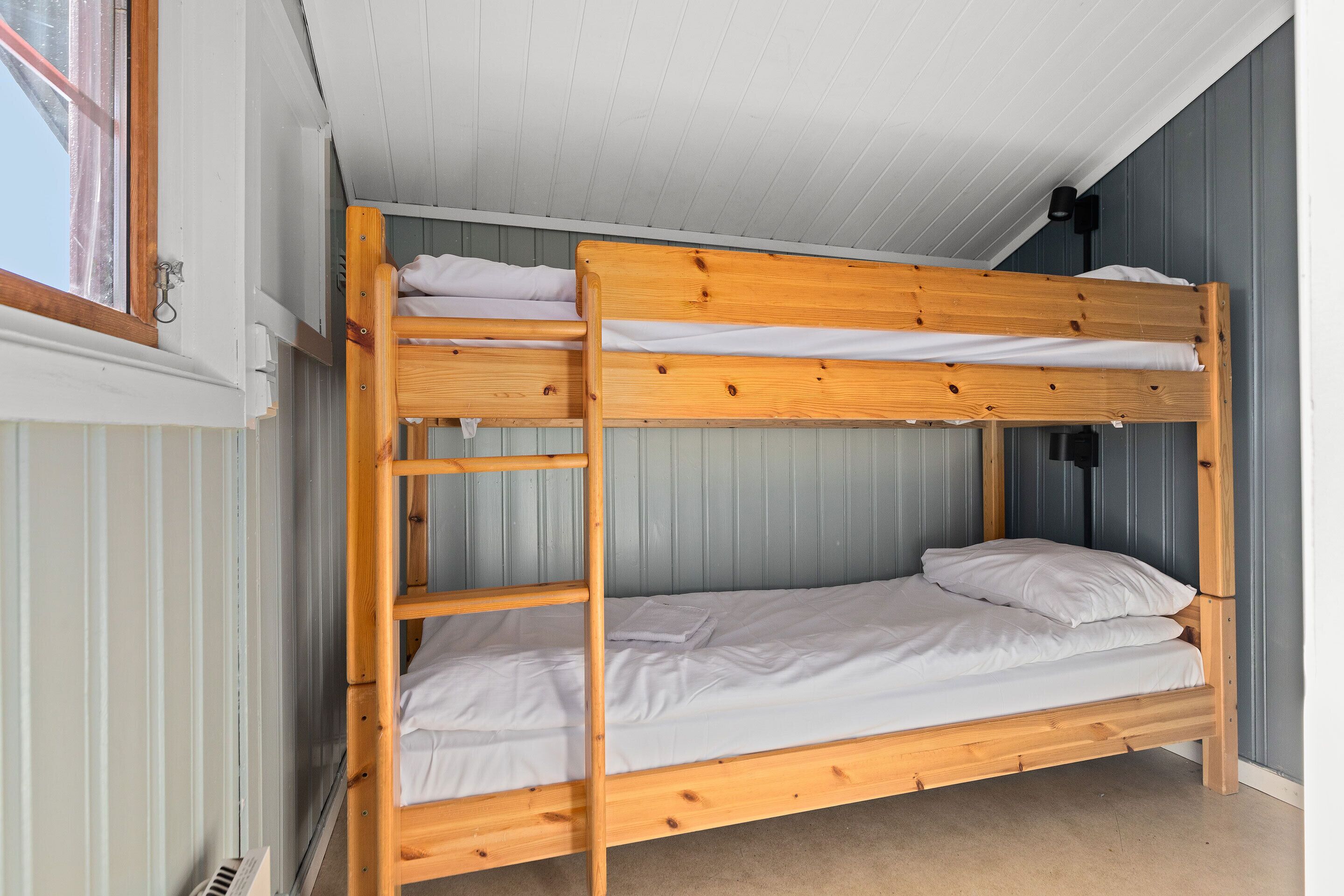 Un letto a castello con biancheria bianca in una stanza con pareti in legno e una finestra.