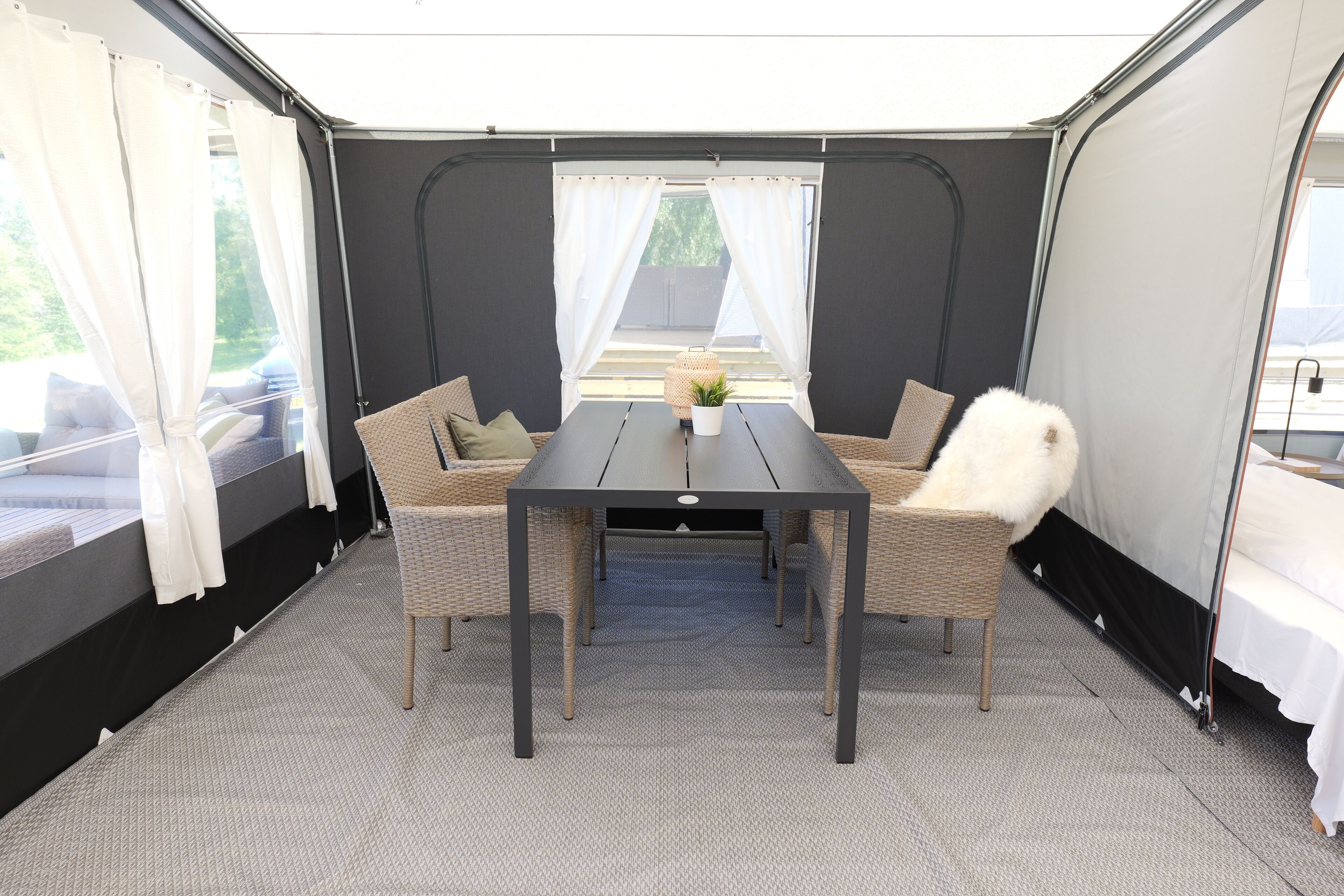 A tented room with a table and two wicker chairs, a white fluffy chair, and a small potted plant.