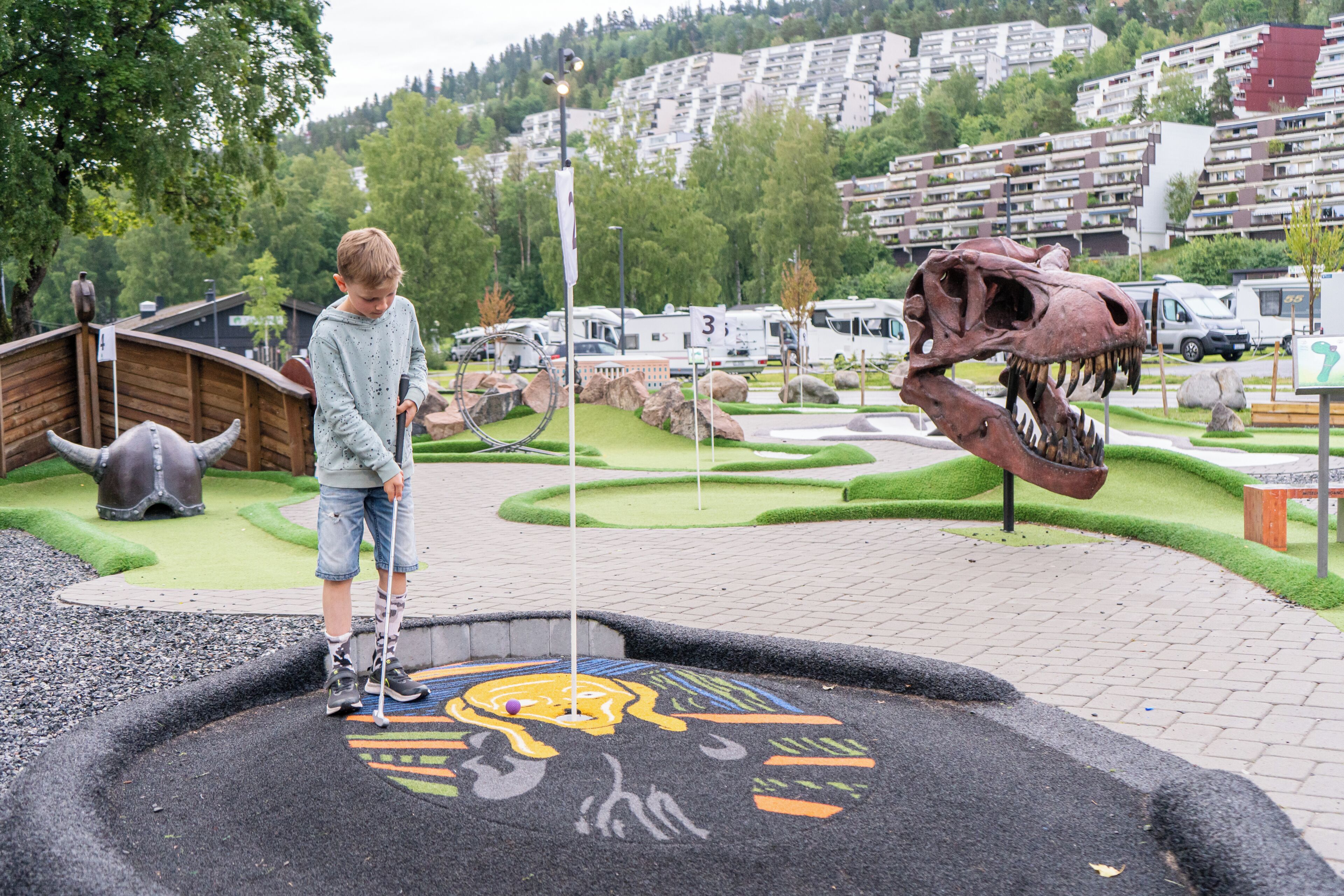 Un enfant joue près du squelette d’un dinosaure dans un parc, avec des camping-cars en arrière-plan.