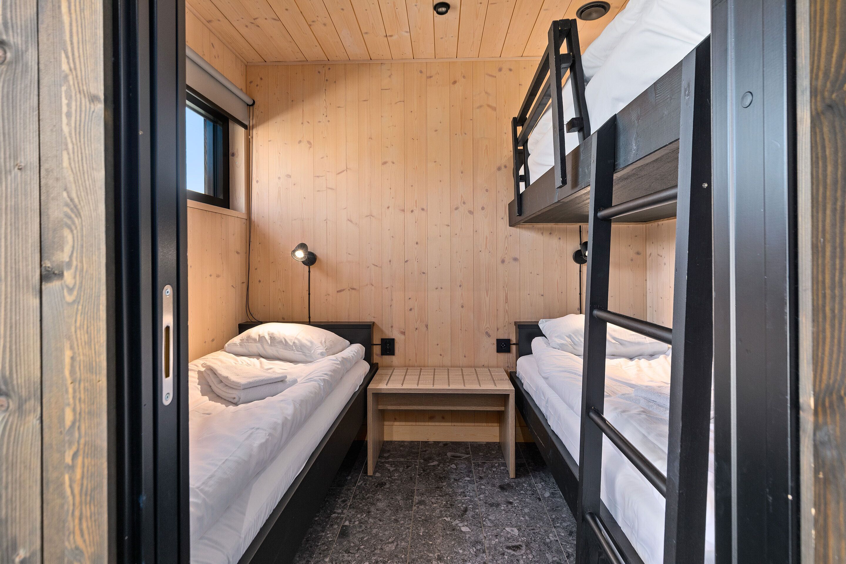 Habitación pequeña con literas, una mesita, una lámpara y una ventana.