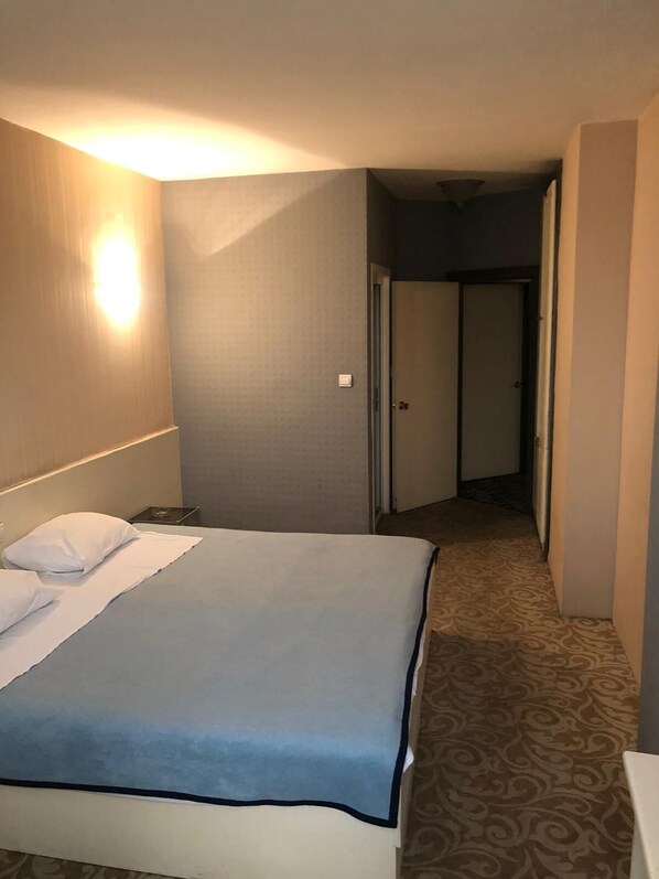 Una habitación de hotel con una cama, una mesita de noche, una lámpara y una puerta que da a otra habitación.