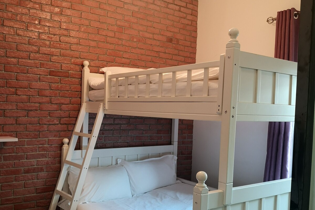 Ein Stockbett mit einer Leiter, weißer Bettwäsche und einer Ziegelwand.