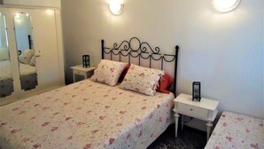 Un dormitorio con una cama, dos mesitas de noche, un espejo y apliques en la pared.