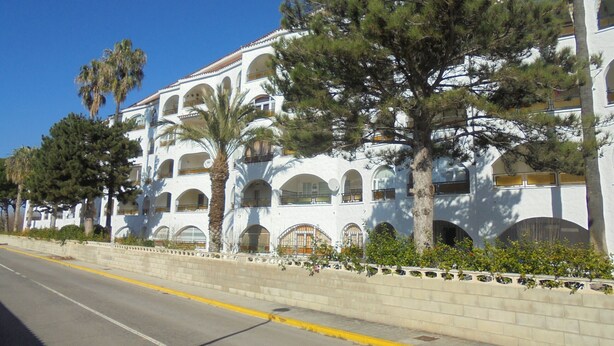 Un edificio blanco con múltiples balcones y ventanas arqueadas, rodeado de árboles y un cielo despejado.