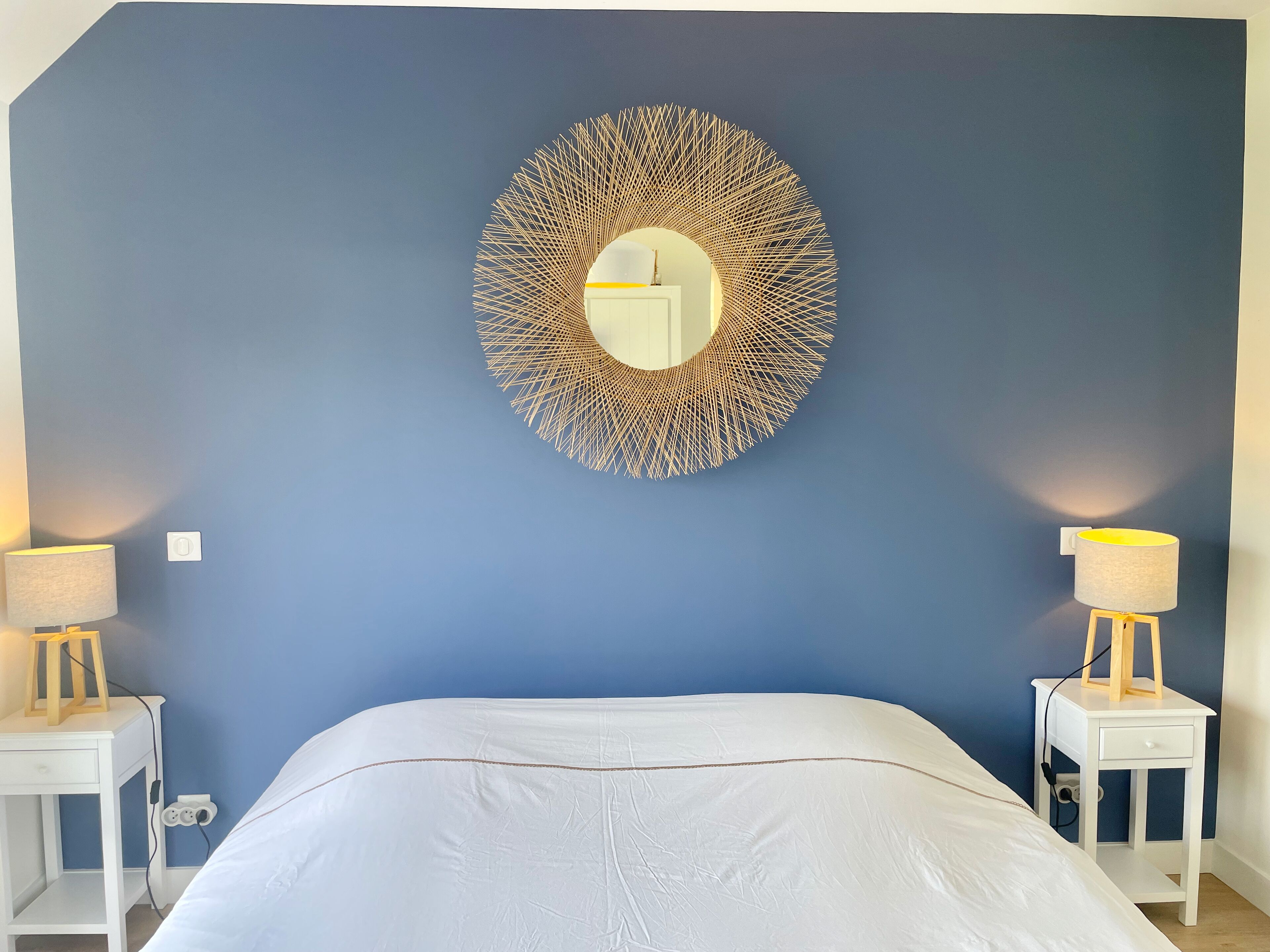 Une chambre à coucher avec un grand lit, deux tables de chevet avec des lampes et un miroir décoratif au mur.