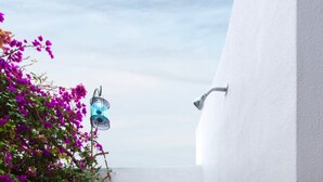 A narrow, white-walled shower area with a tiled floor, a metal showerhead, and a blue light fixture. - Acropolis Lindos Home (Rhodes)
