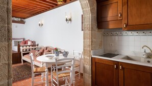 A cozy kitchen with wooden cabinets, a white countertop, and a dining area with a table and chairs. - Acropolis Lindos Home (Rhodes)