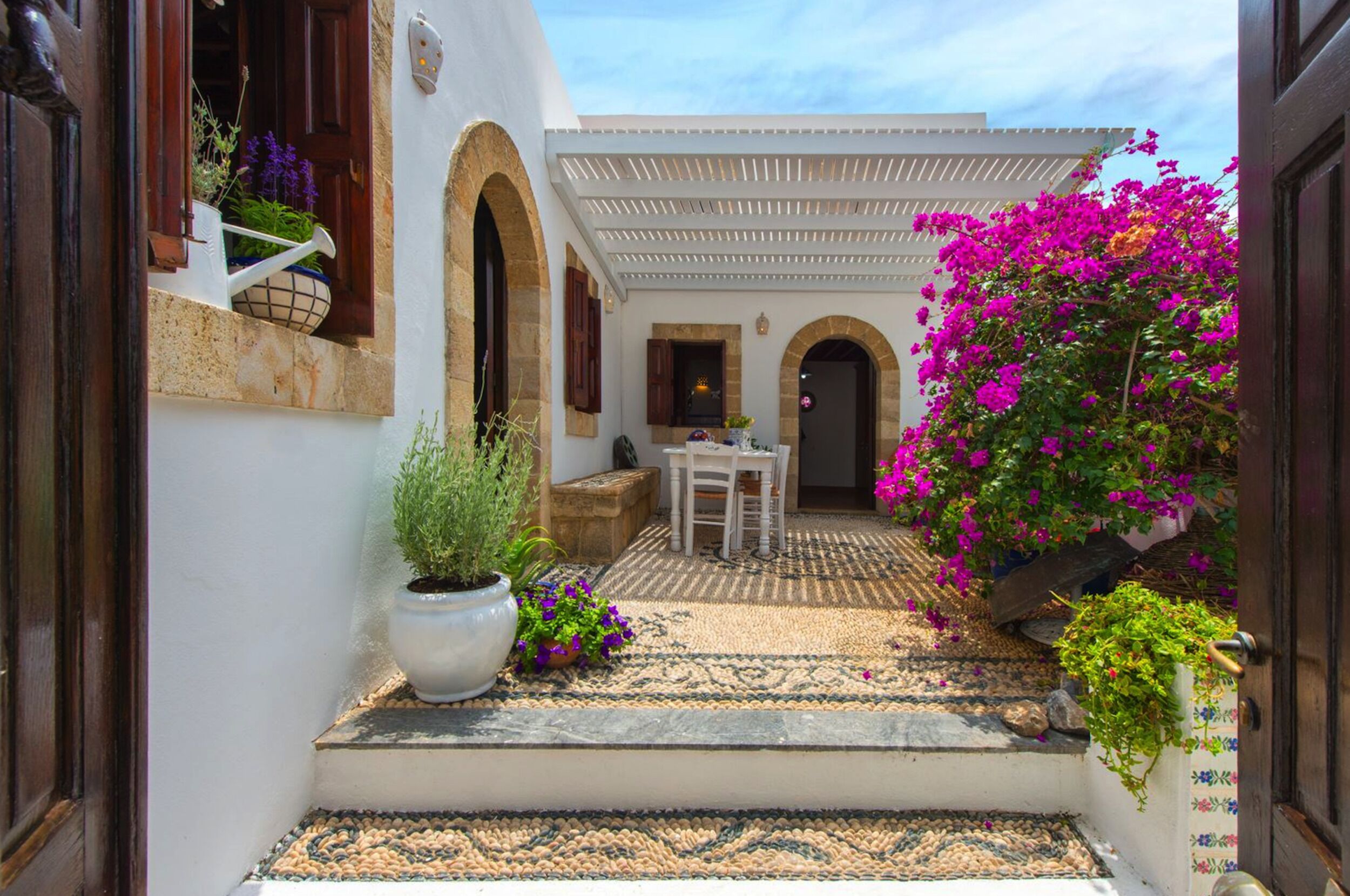 A courtyard with a white building, a table with chairs, and potted plants.