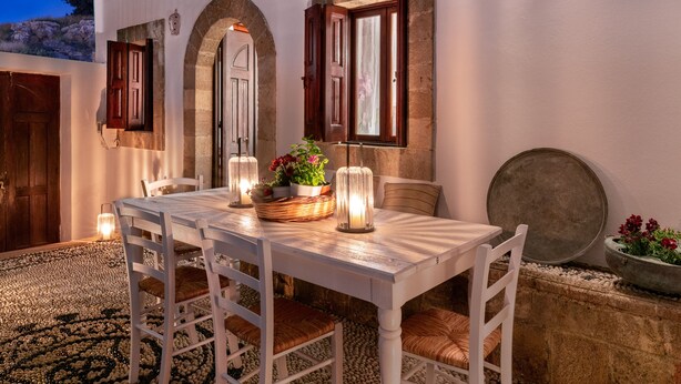 A dining area with a white table and chairs, a basket with flowers, and a candle. - Acropolis Lindos Home (Rhodes)