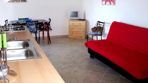 Un espacio habitable compacto con kitchenette, zona de comedor, sofá rojo, televisor y una obra de arte floral en la pared.
