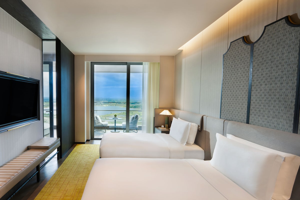 Une chambre d’hôtel avec deux lits, une télévision, un balcon avec vue et un mur décoré de motifs.