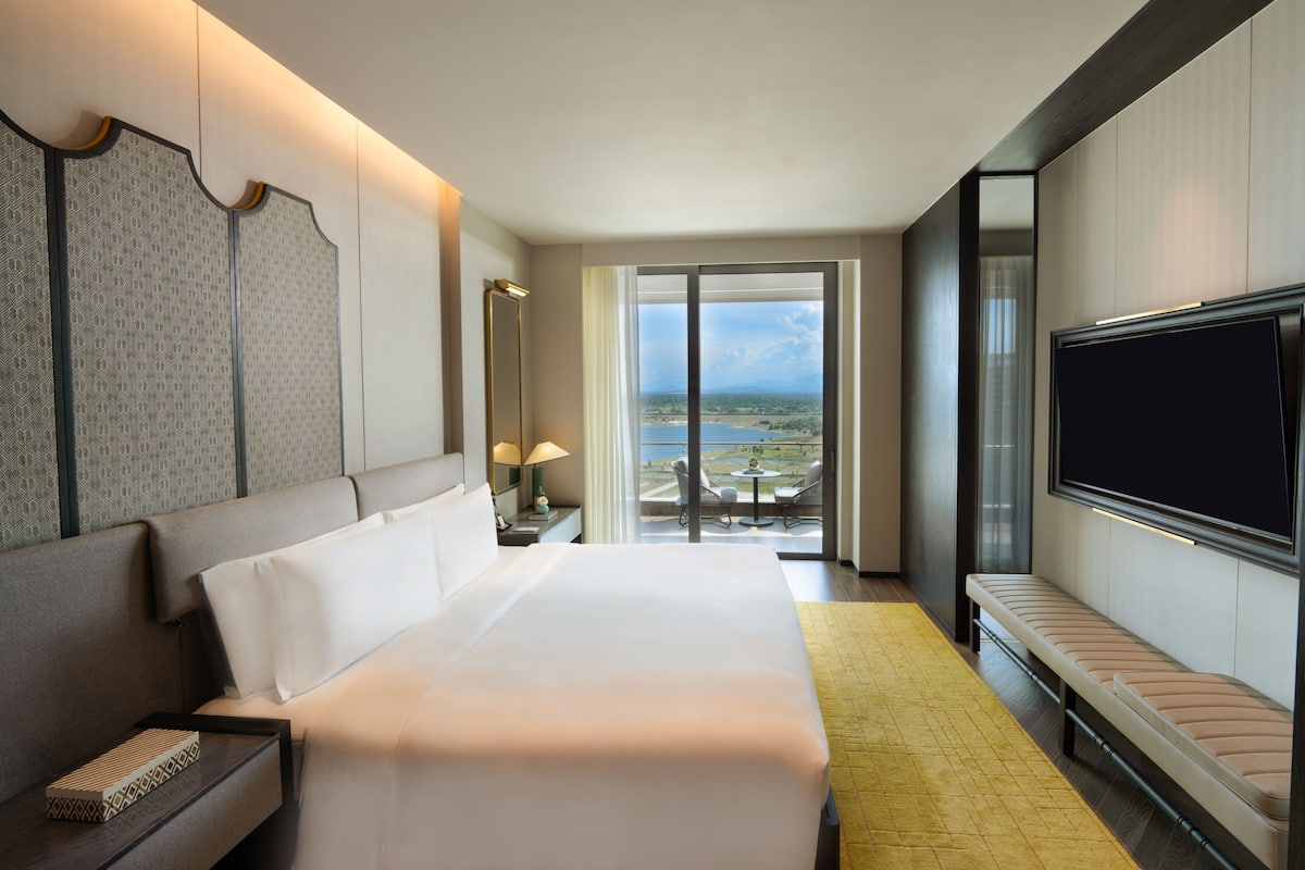 Une chambre d’hôtel avec un grand lit, une télévision, un balcon donnant sur le paysage et un bureau avec une lampe.
